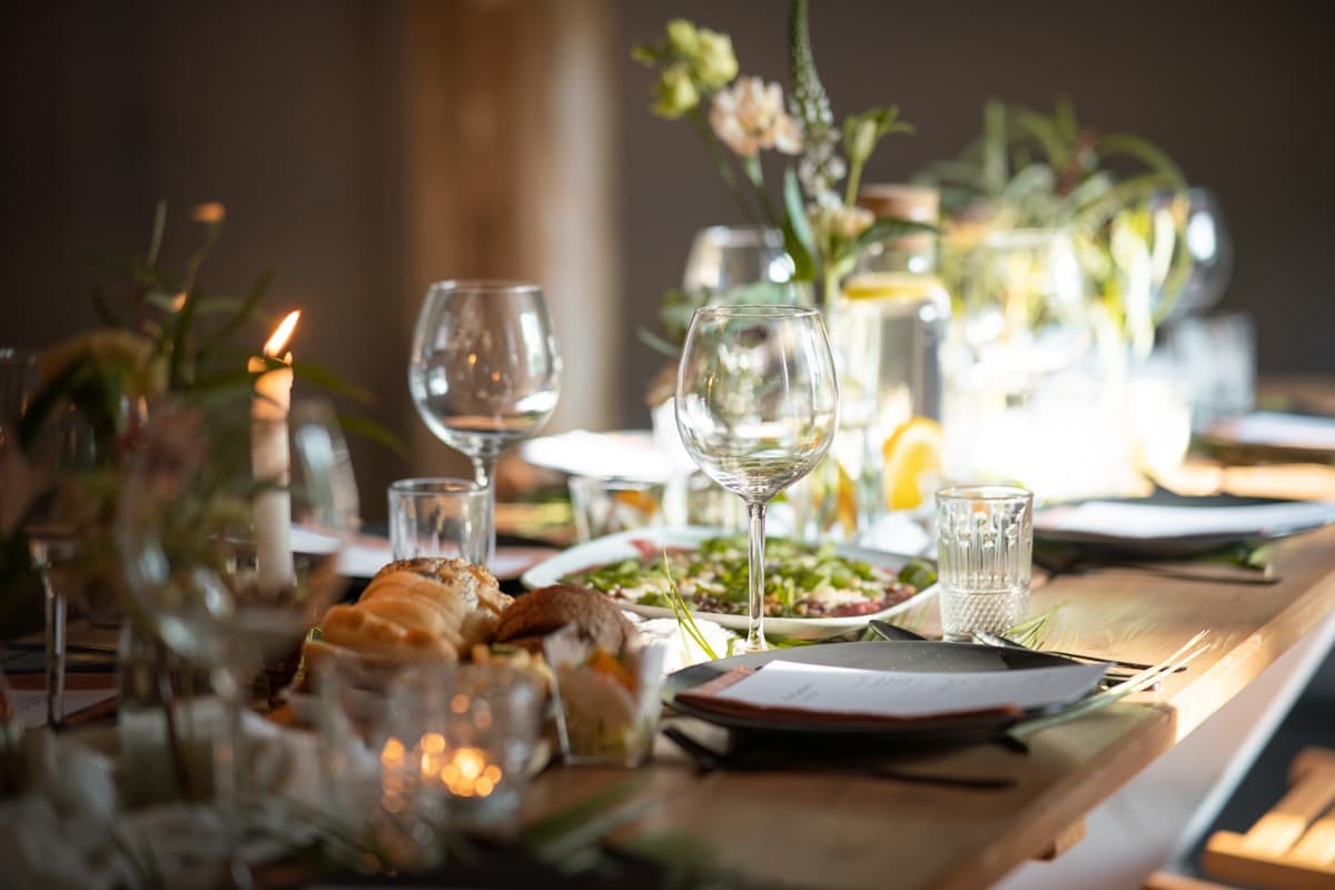 A long dinner table set with wine glasses, candles and low greenery in warm evening light.